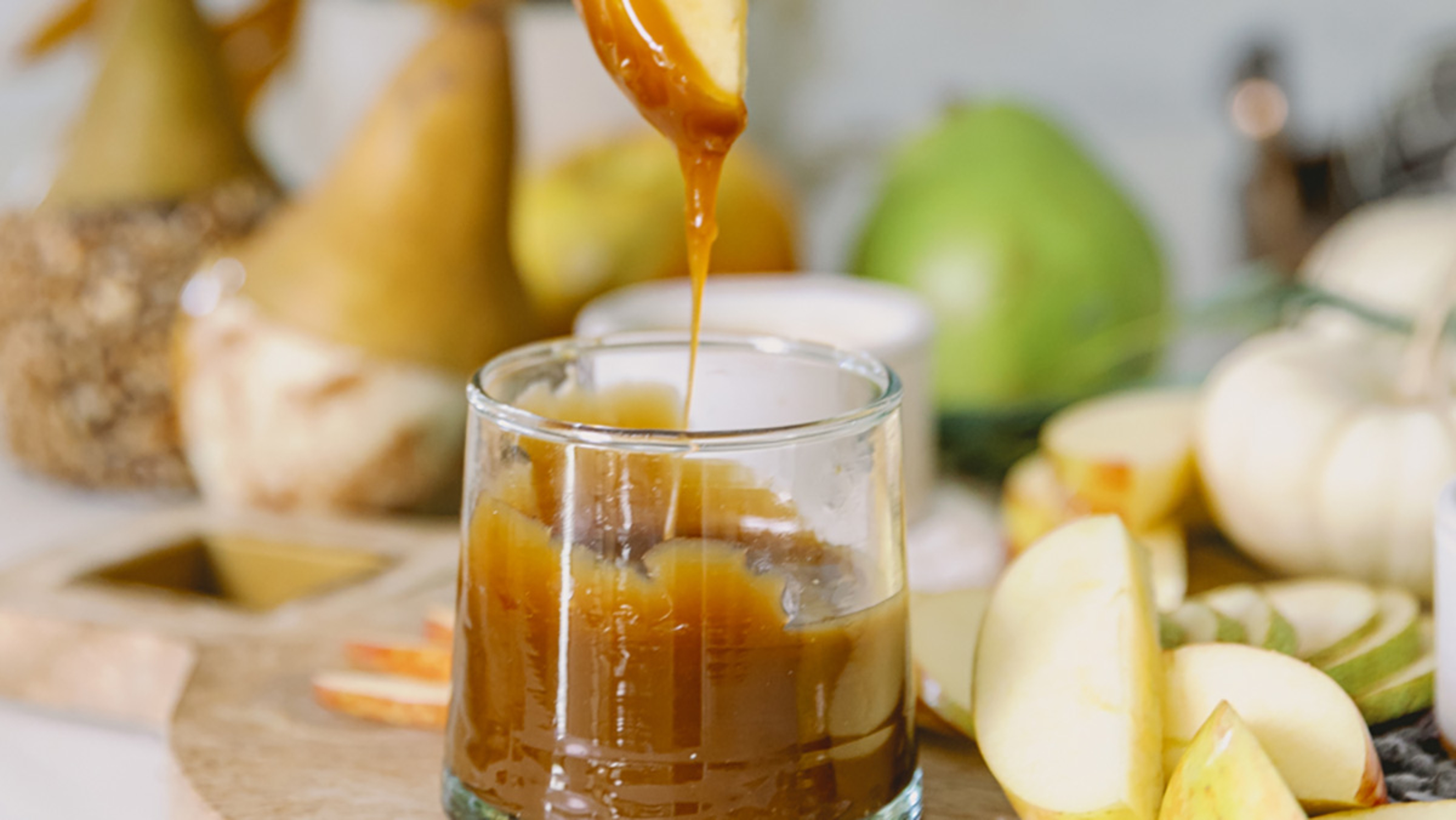 Apple slice dripping with caramel over a pot of caramel sauce.