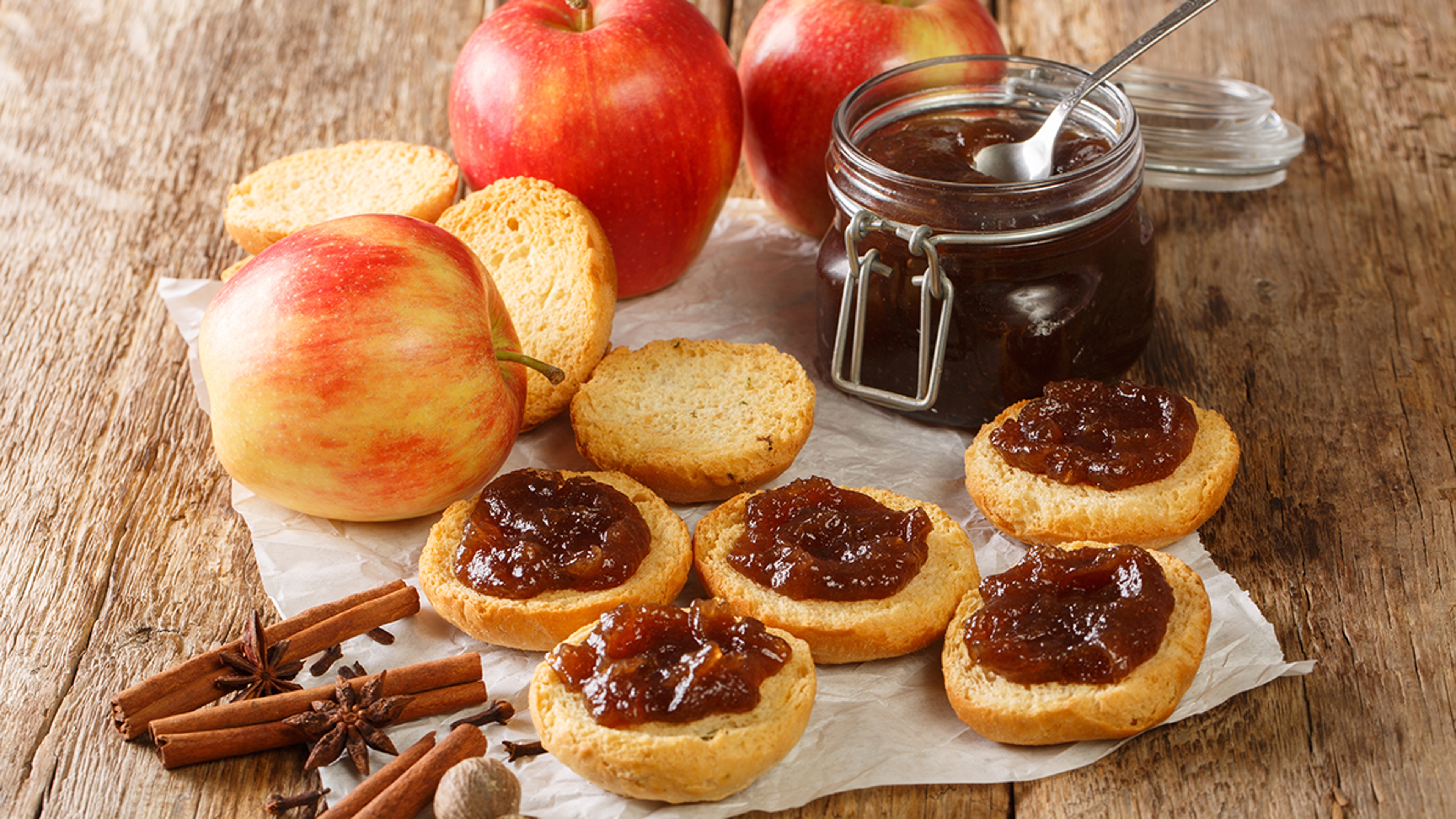 Apple butter recipes with a jar of apple butter next to several pieces of toast and ripe apples.