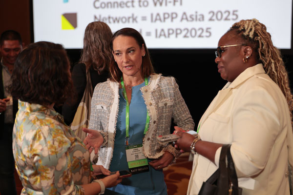 Conference session with a speaker presenting at a podium in front of a large screen displaying event branding and session details.