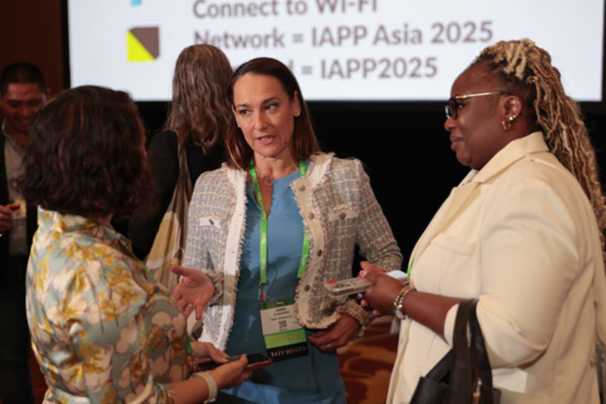 Conference session with a speaker presenting at a podium in front of a large screen displaying event branding and session details.