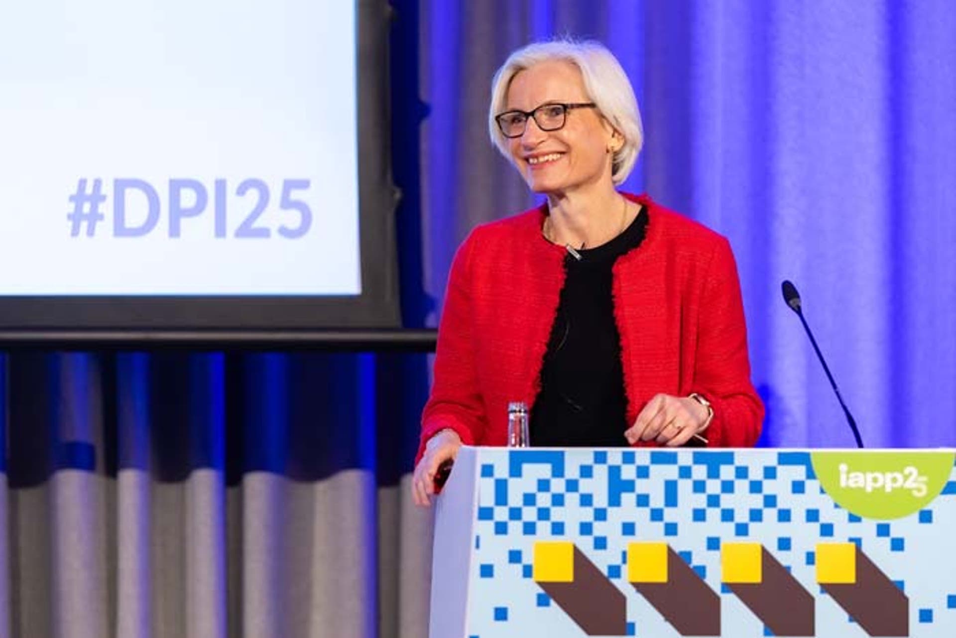 A woman in a red jacket speaking at a podium