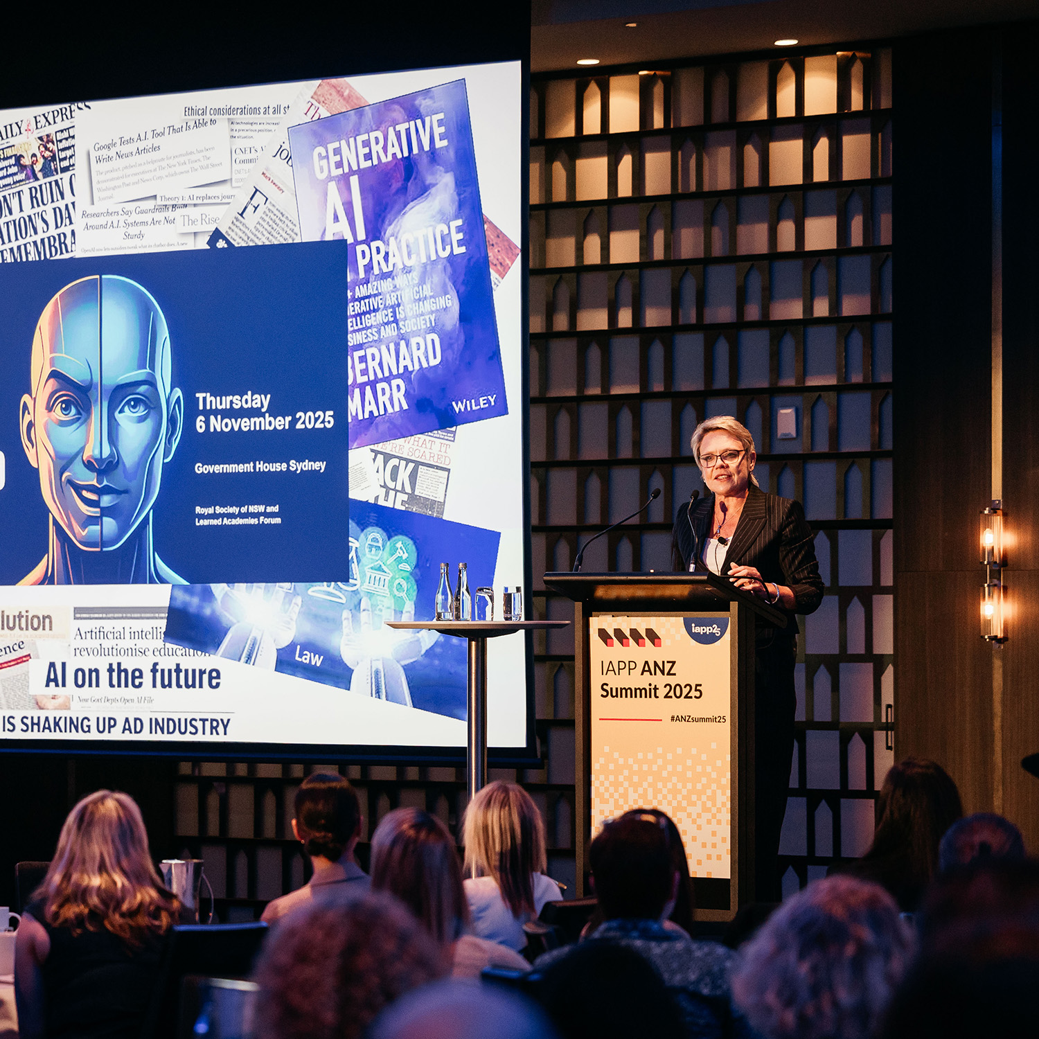 Speaker at a podium presenting in front of a large screen with the headline “AI: The Hope and The Hype” and related graphics.