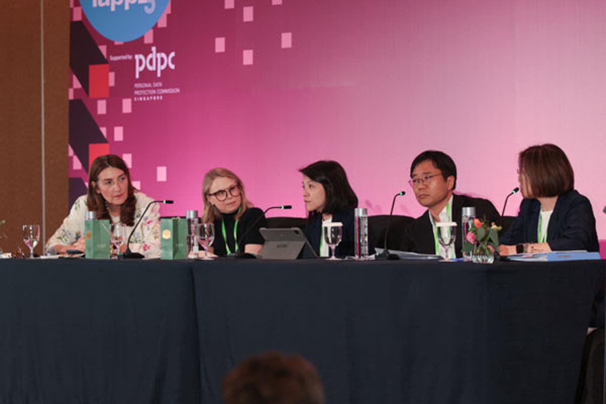 Networking area with attendees gathered around a tall table, holding drinks and engaging in conversation. Event signage is visible in the background.