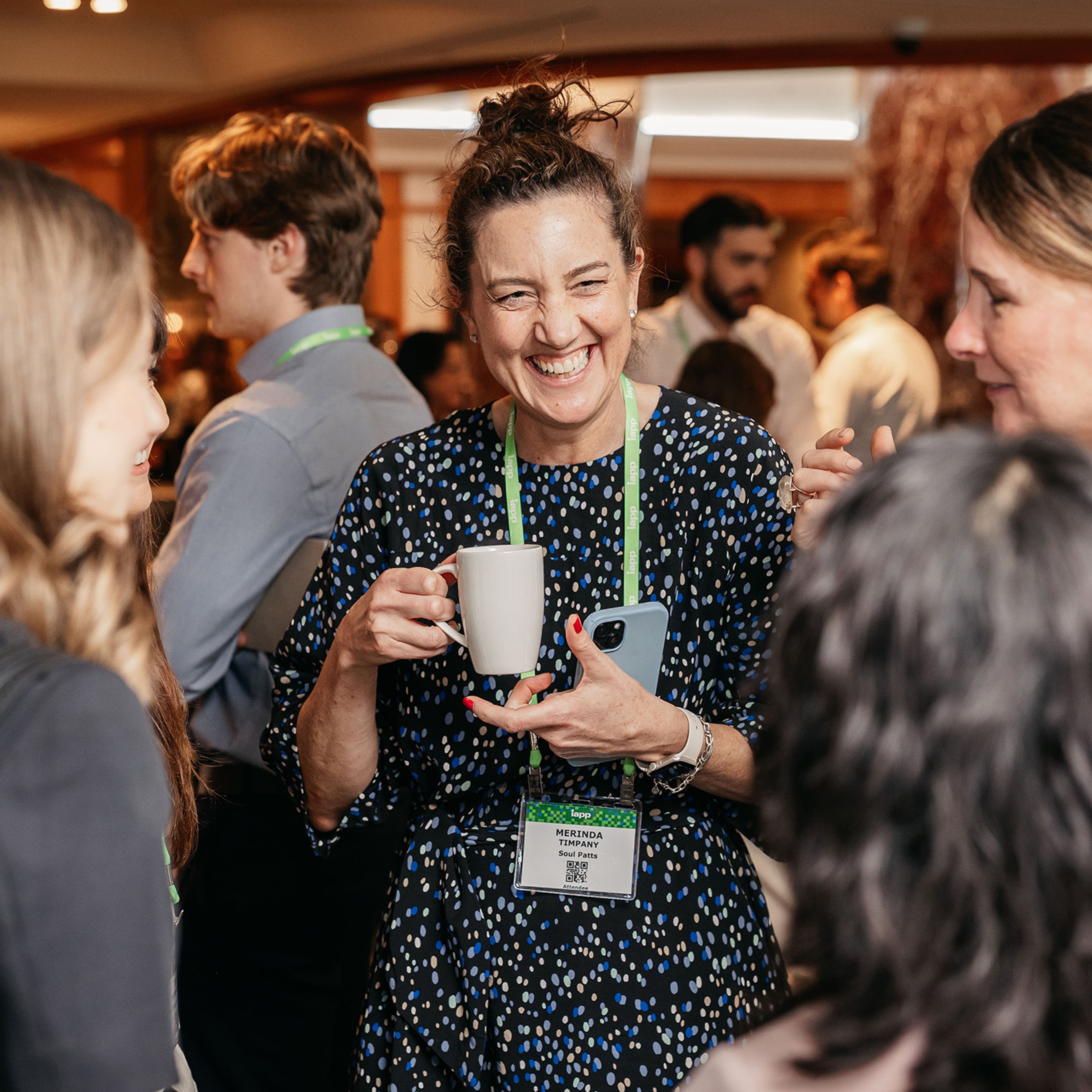 Attendee holding a coffee cup and smartphone during a networking session in a crowded room.
