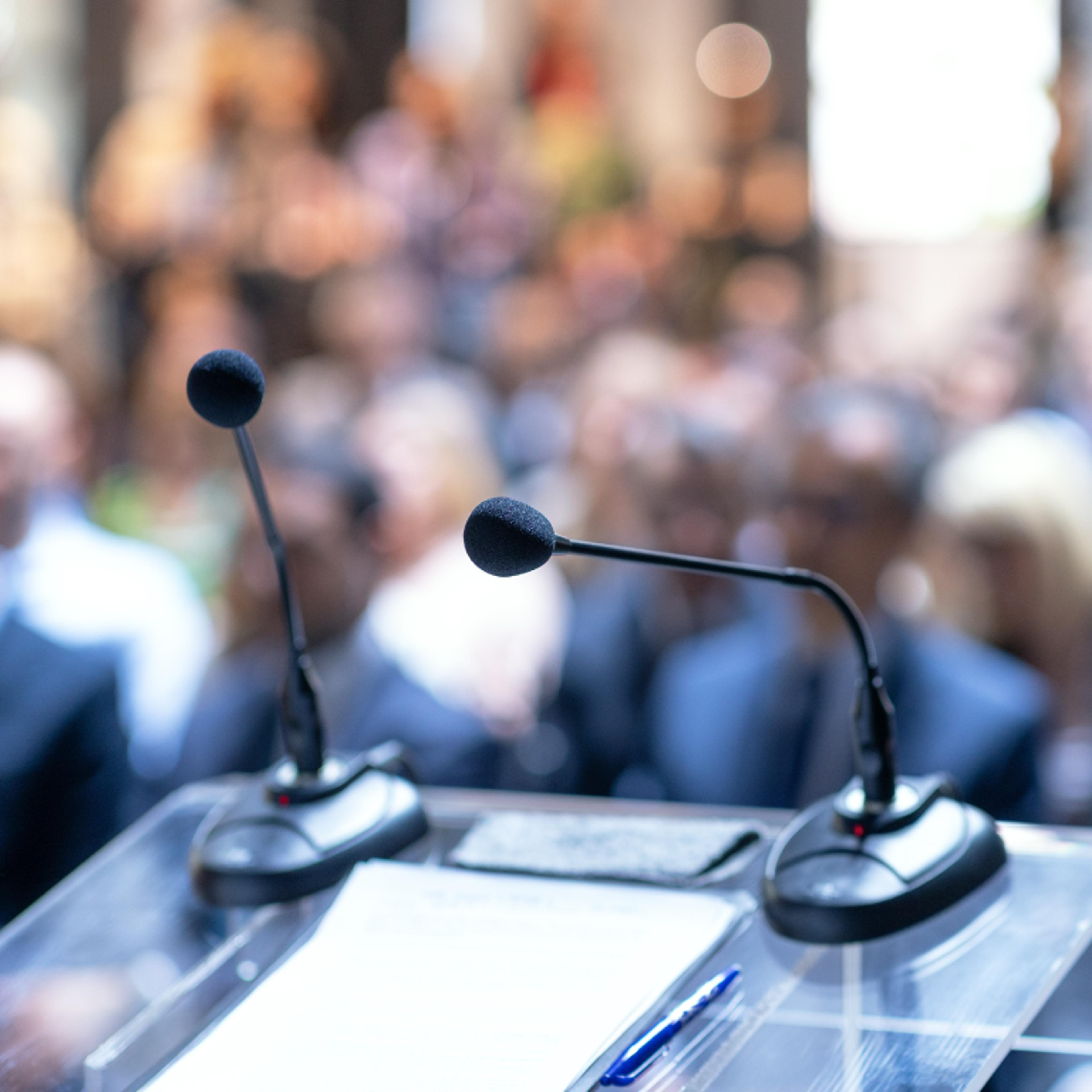 Image of two microphones in front of a crowd of people