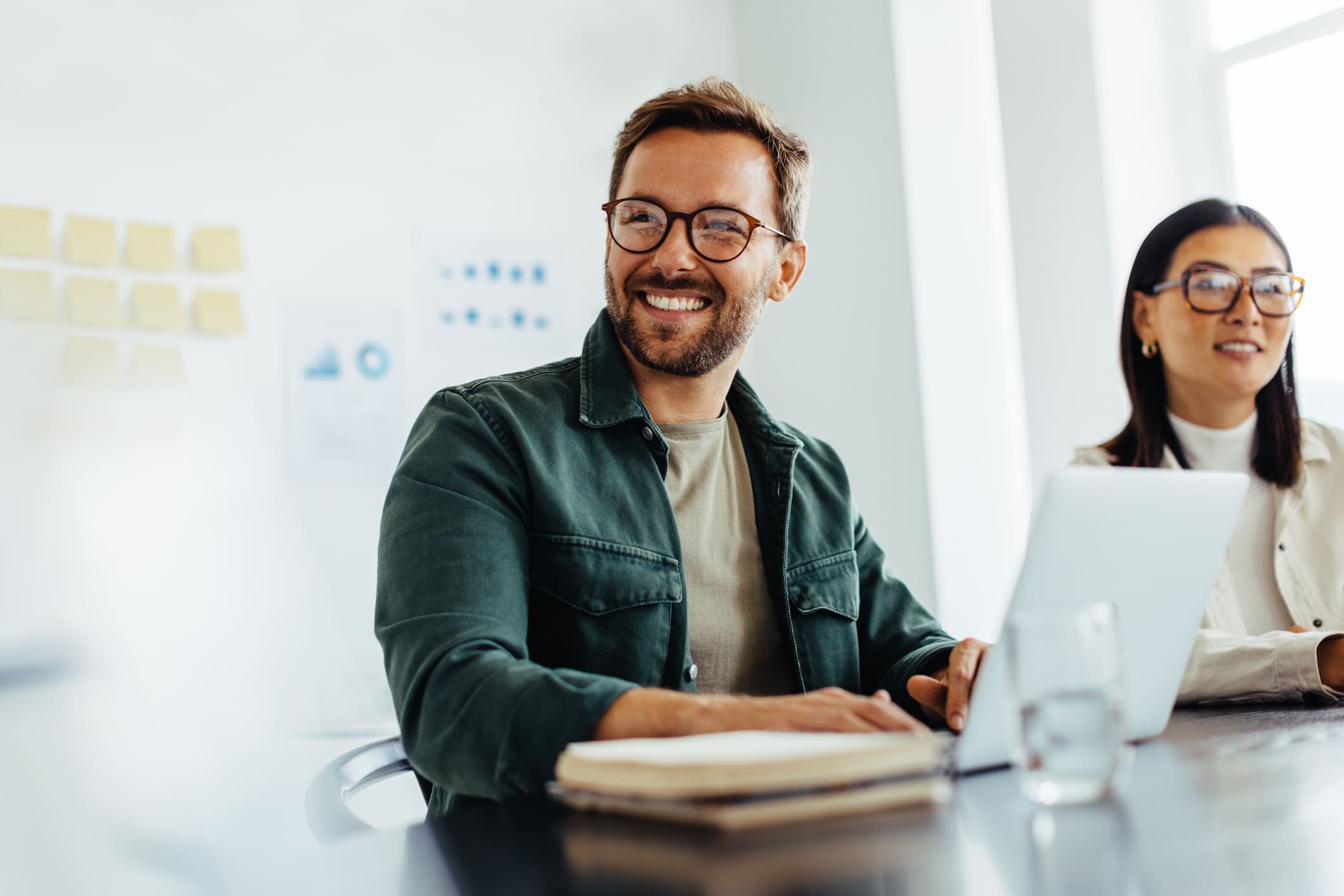 person smiling and working at a desk with laptop and notebook