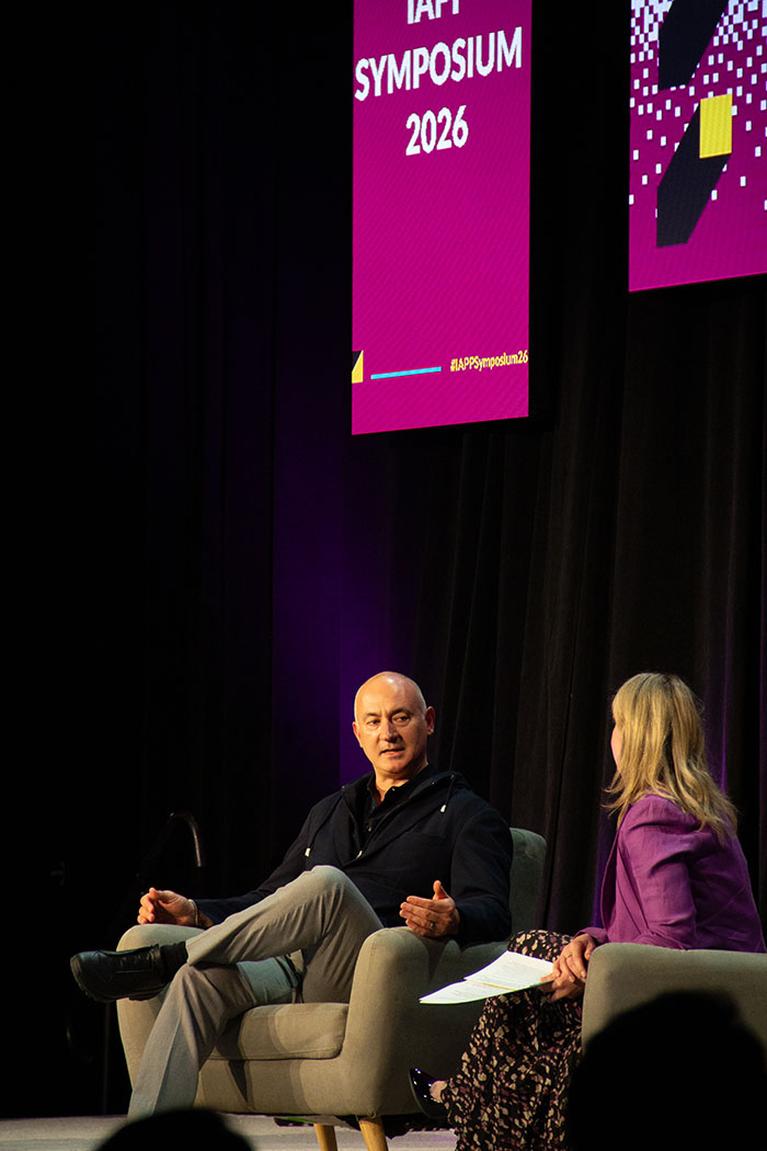Onstage interview at IAPP Symposium 2026 featuring two speakers seated in armchairs, engaged in discussion beneath tall pink event signage.