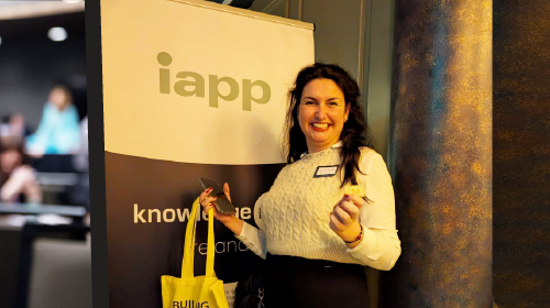 A person standing beside an IAPP banner while holding a yellow tote bag in a conference setting.