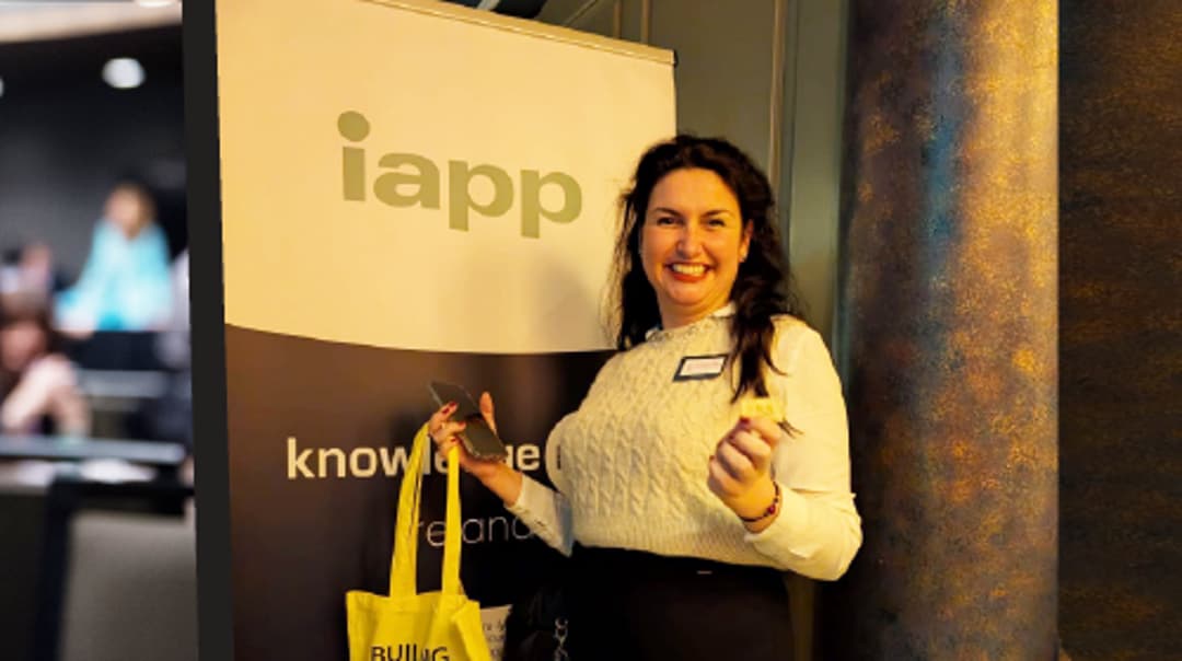A person standing beside an IAPP banner while holding a yellow tote bag in a conference setting.