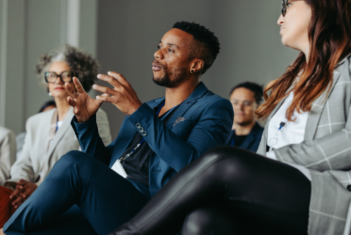 An African-American man in a blue suit sitting with his legs crossed and speaking. He is gesturing with his hands.