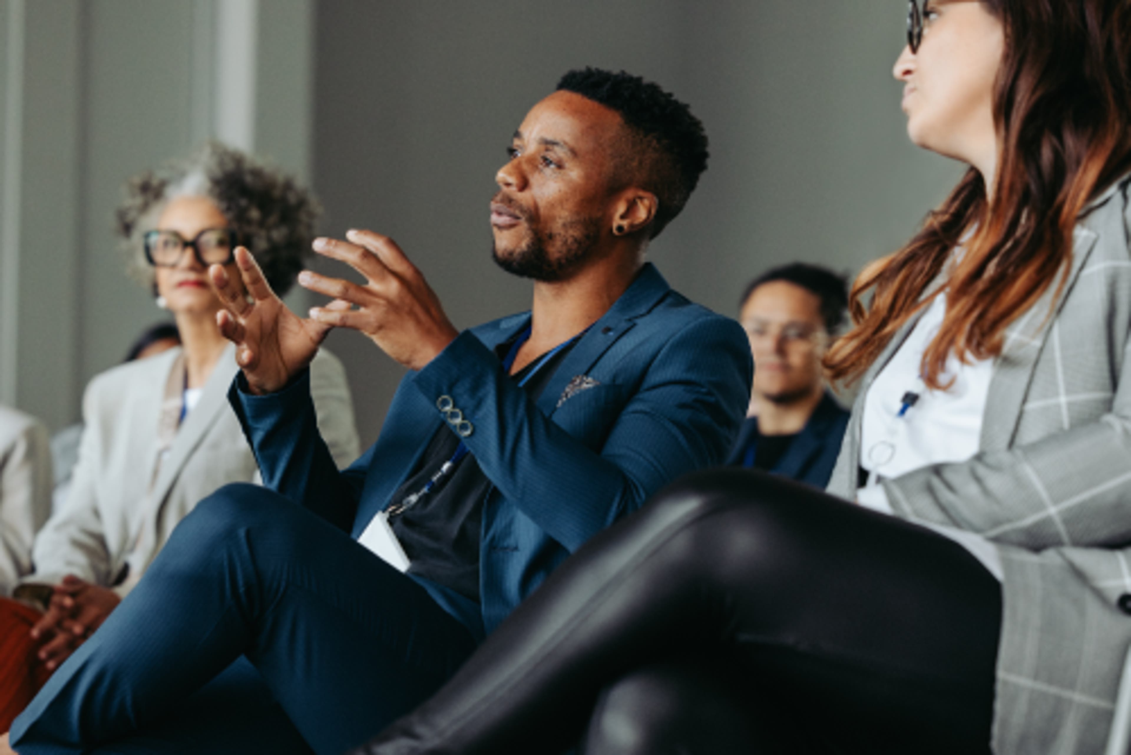 An African-American man in a blue suit sitting with his legs crossed and speaking. He is gesturing with his hands.