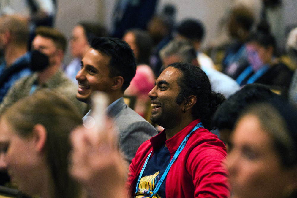 An African-American man in a blue suit sitting with his legs crossed and speaking. He is gesturing with his hands.