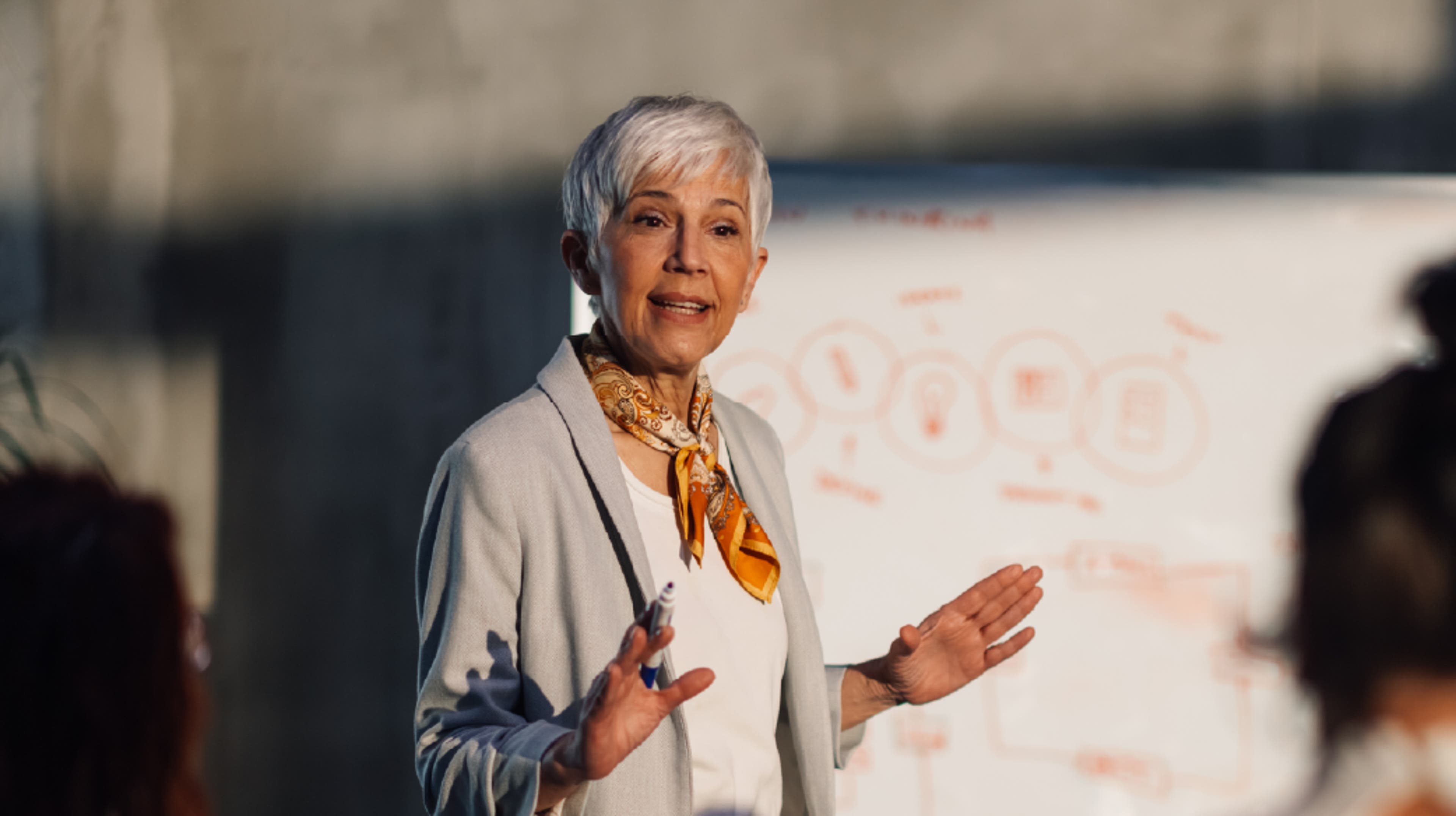 A woman in a grayish-white jacket giving a presentation.