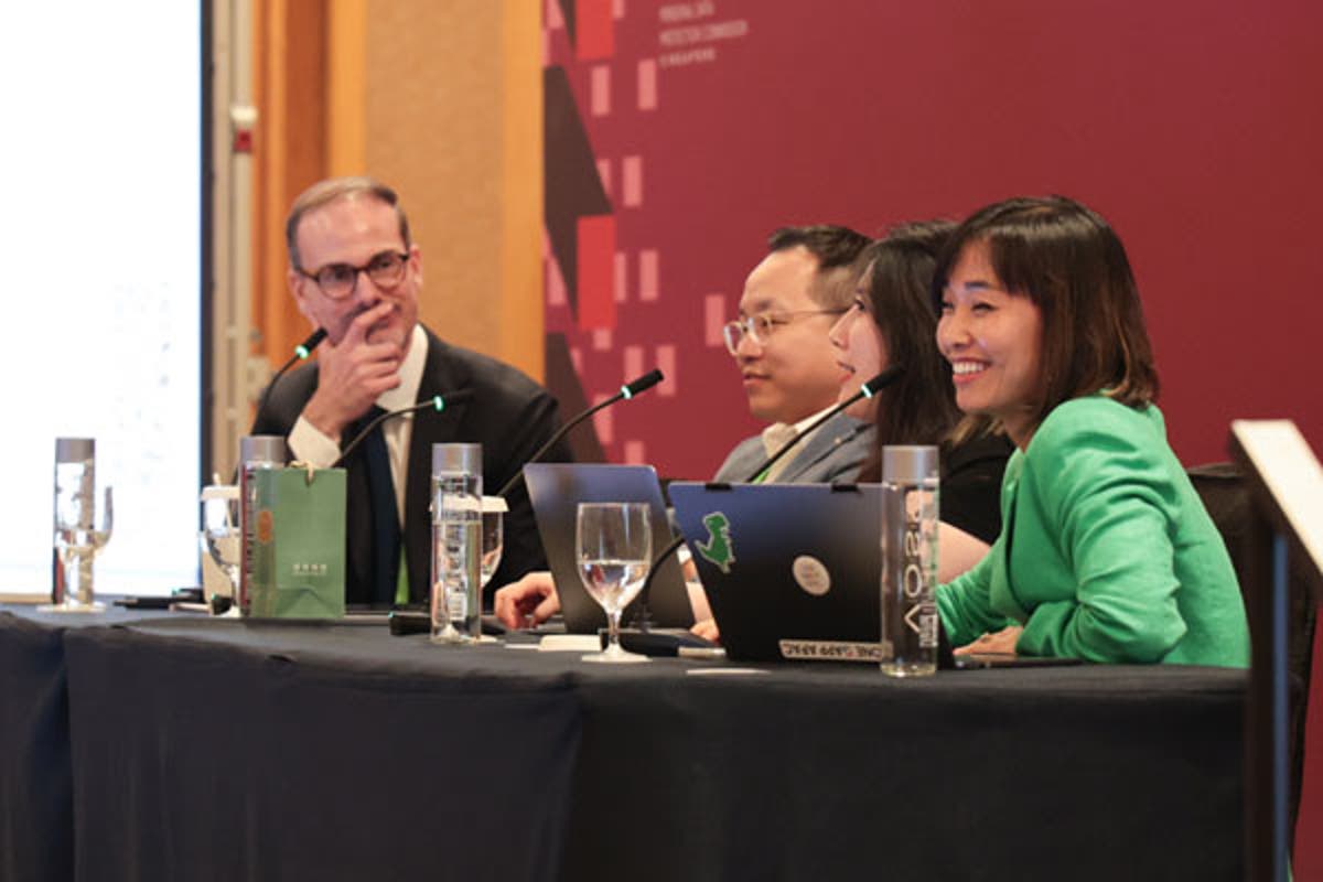 Conference room with a speaker presenting at a podium in front of two large screens displaying a circular AI governance framework diagram.