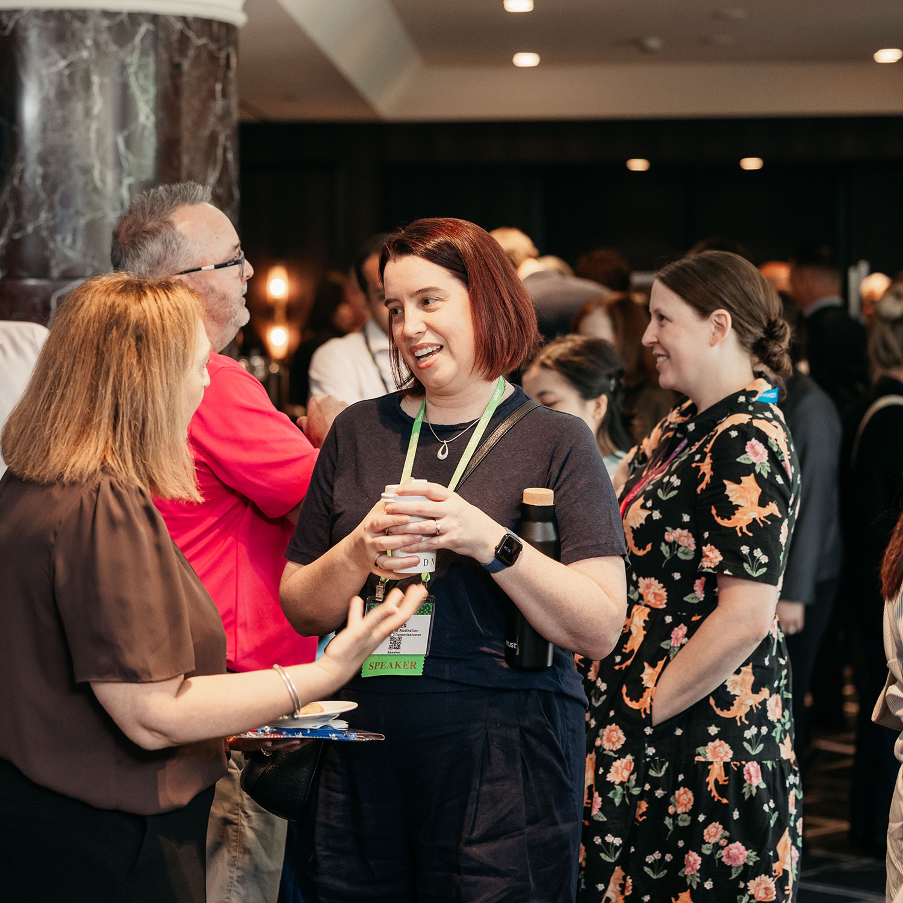 Networking area with attendees standing in small groups and talking near a blue display wall.