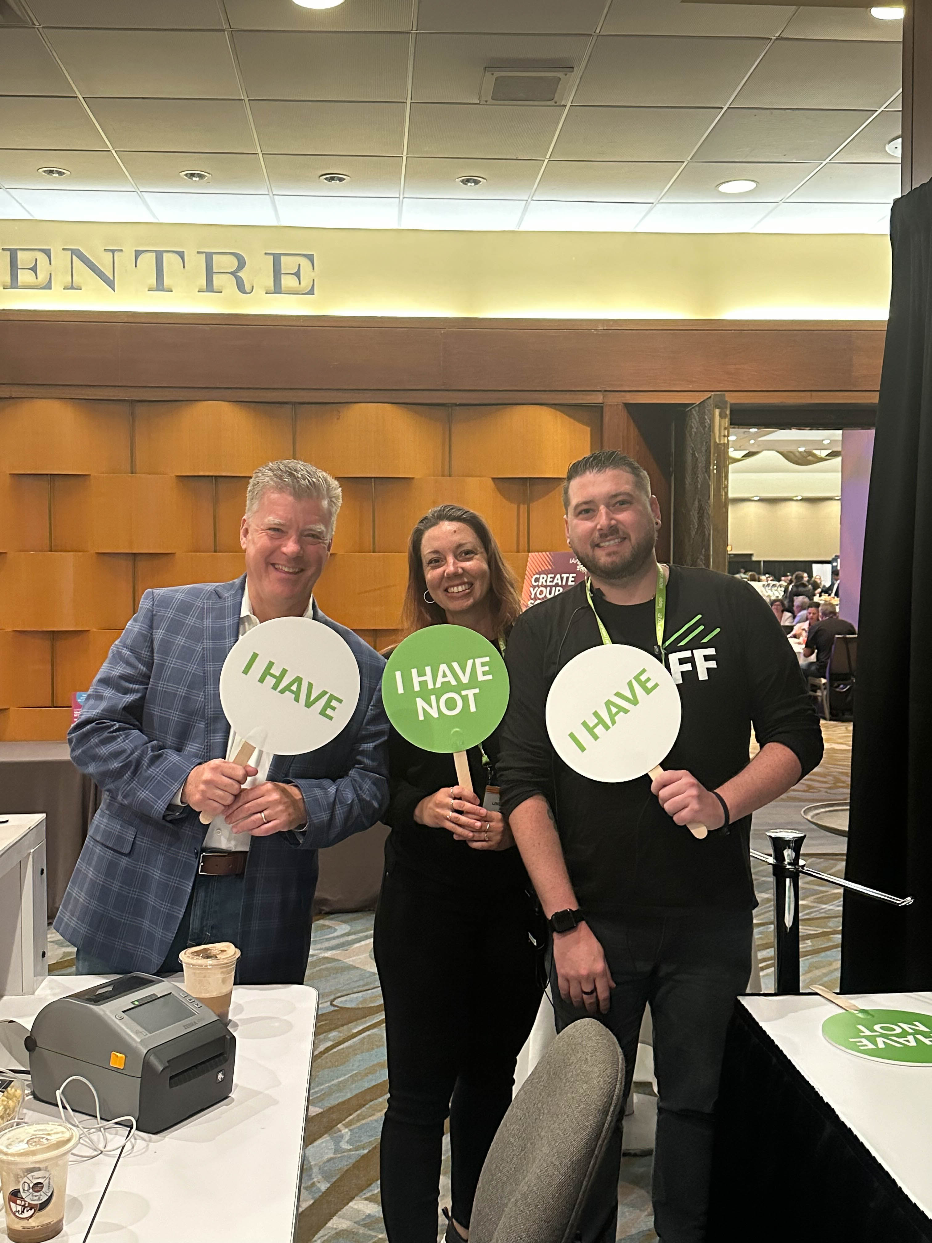 Three people standing together holding small circular signs reading "I have," "I have not" and "I have"