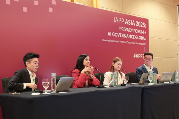 Exhibit booth with attendees interacting at a counter displaying brochures, pens, and branded items. A banner highlights privacy and data management solutions.
