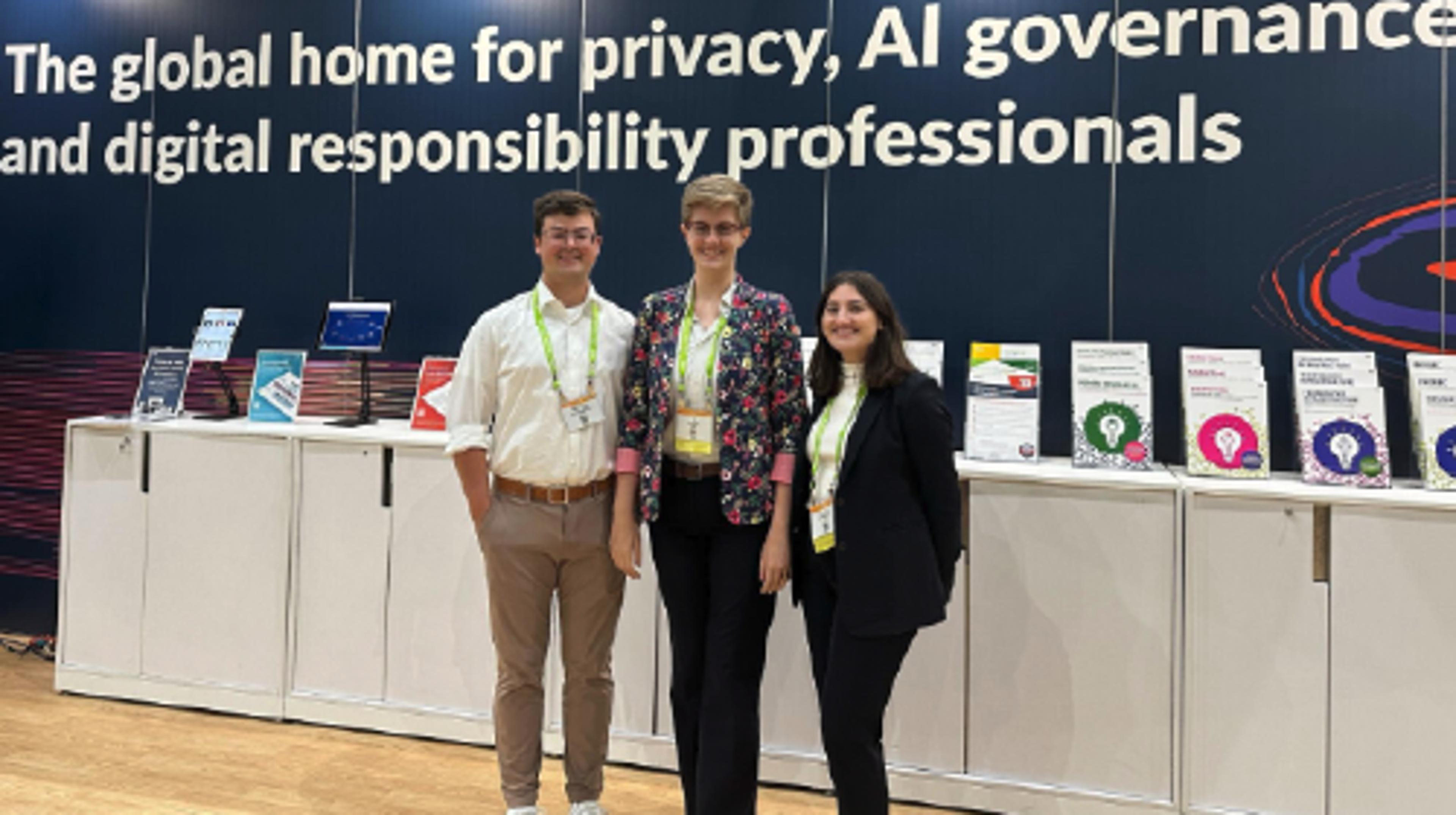 Three people standing in front of a booth with a sign behind them reading The Global Home for Privacy, AI Governance and Digital Responsibility Professionals