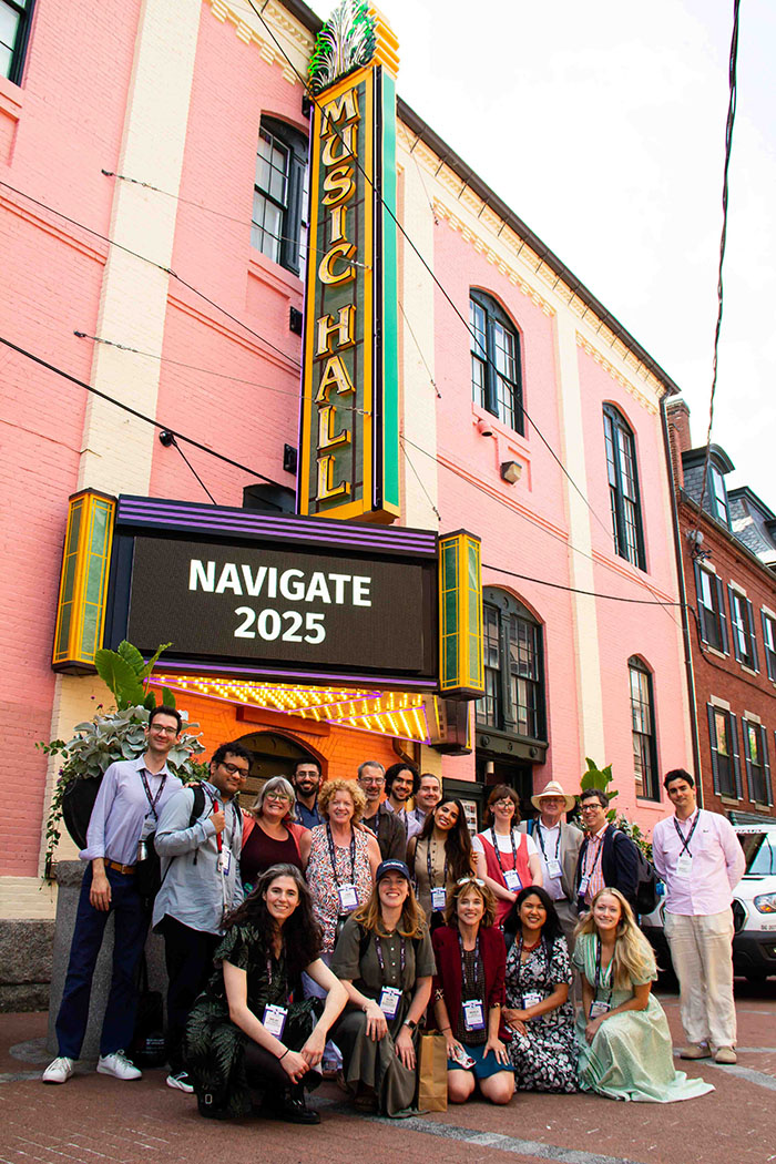 Large group posing in front of a pink building with a marquee reading “Music Hall” and “Navigate 2025.”