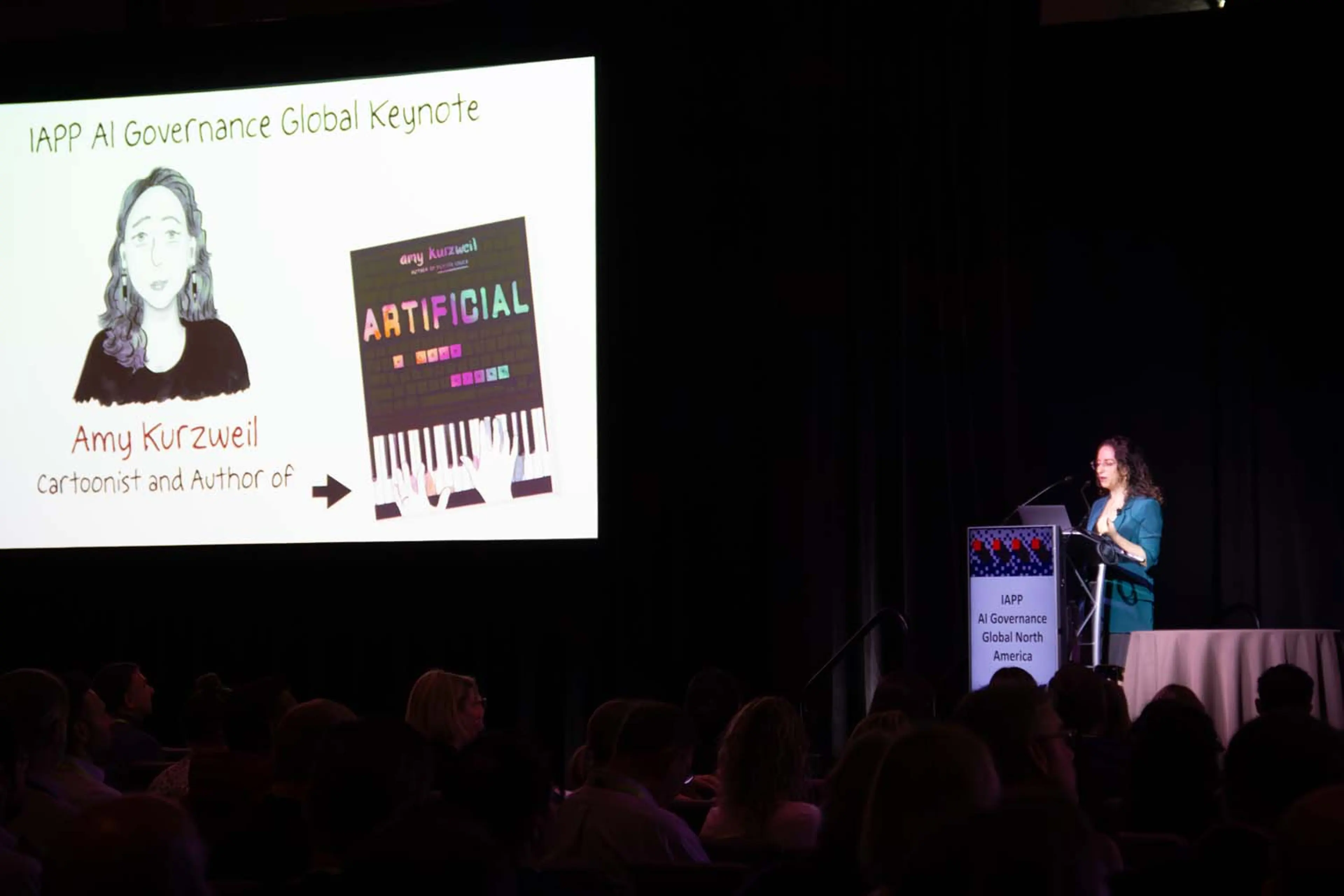 A keynote speaker stands beside a large projected slide reading “IAPP AI Governance Global Keynote,” which features an illustration and book cover as the audience watches from darkened seating.