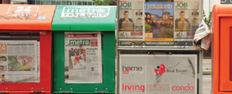 A collection of urban newspaper stands and racks displaying headlines and magazine covers.