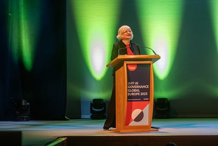 Speaker at a podium on stage with signage reading “IAPP AI Governance Global Europe 2025.” Green lighting illuminates the backdrop.