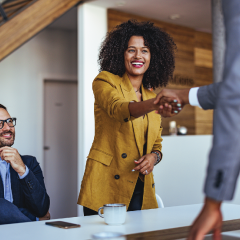 A woman standing and reaching across a table to shake someone's hand