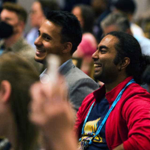 Two young men sitting in the audience of an IAPP conference session. They are listening to the speaker and smiling.