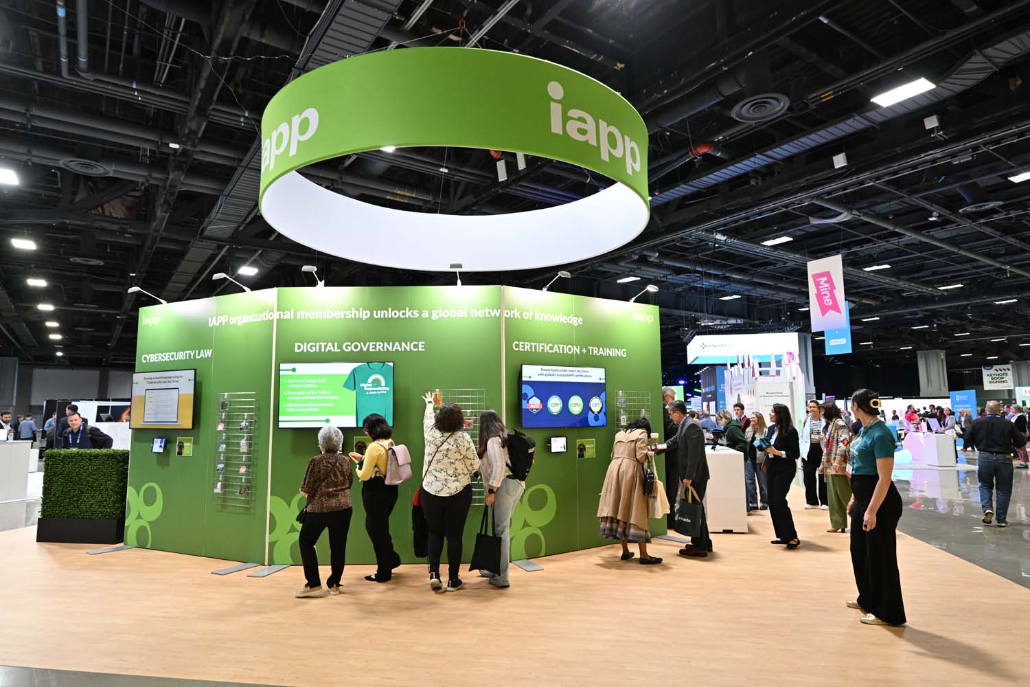 A large IAPP exhibition booth dominates the show floor, displaying sections labeled Cybersecurity Law, Digital Governance, and Certification and Training as attendees browse screens and materials.