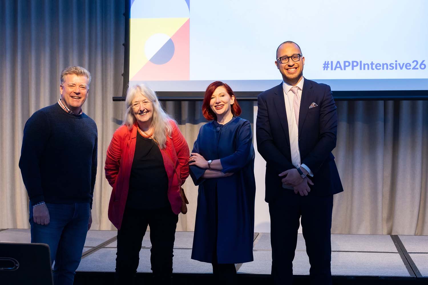 Four speakers stand side by side on a stage beneath a large screen displaying IAPP Intensive 2026 branding. The group faces the audience in a conference presentation space.