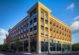Brick hotel building with large windows and ground-floor retail space under a clear blue sky.