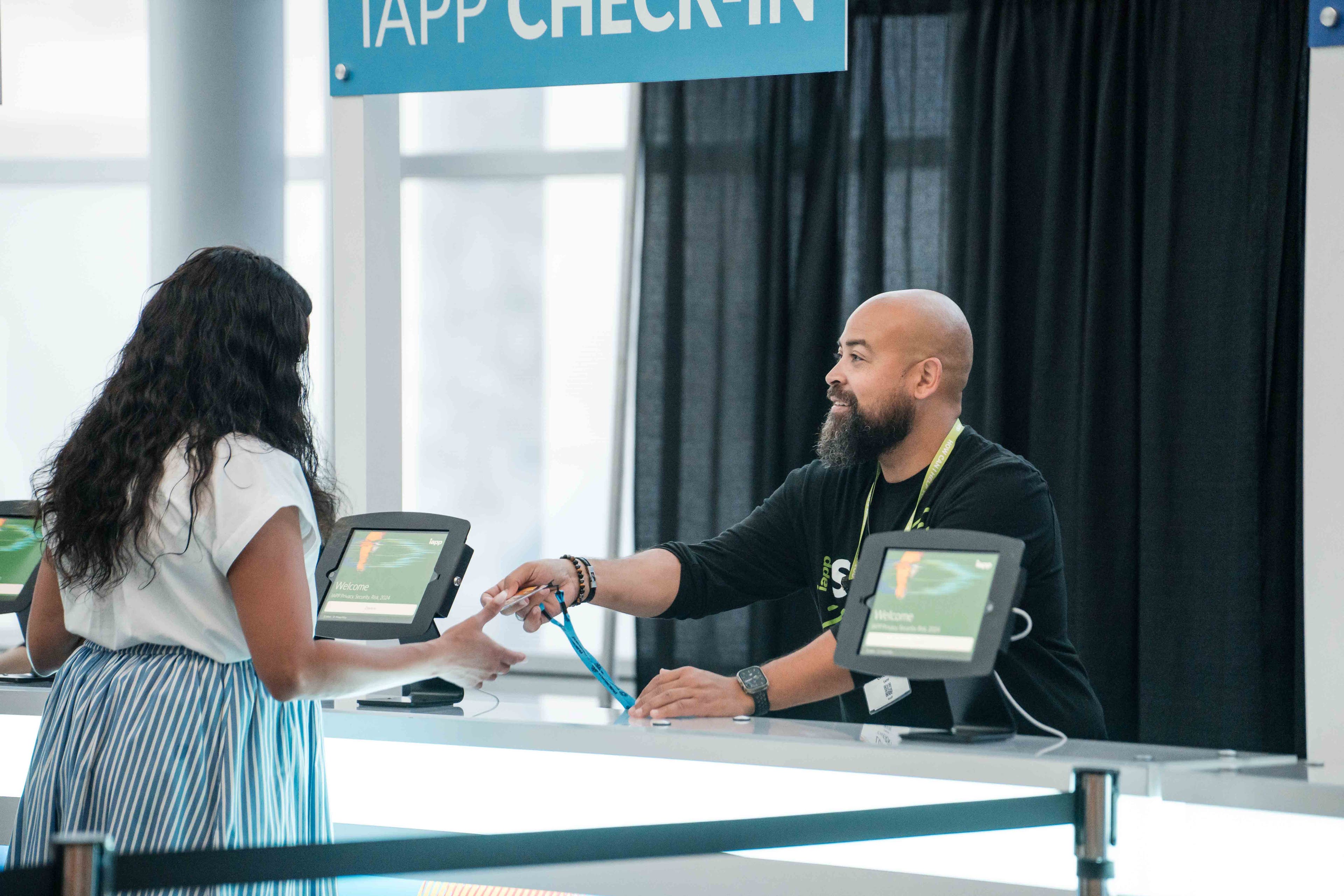A man with a beard at an information booth assisting a conference attendee