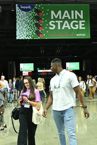 Two attendees walking in a large convention hall under a green banner that reads “MAIN STAGE.” Other people and directional signs are visible in the background.