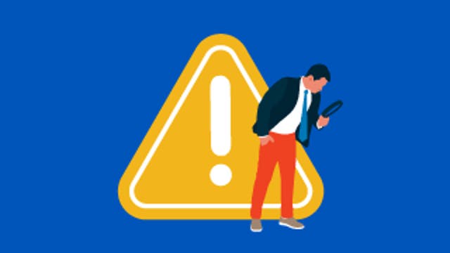 Person examining a phone in front of a large yellow warning triangle with an exclamation mark.