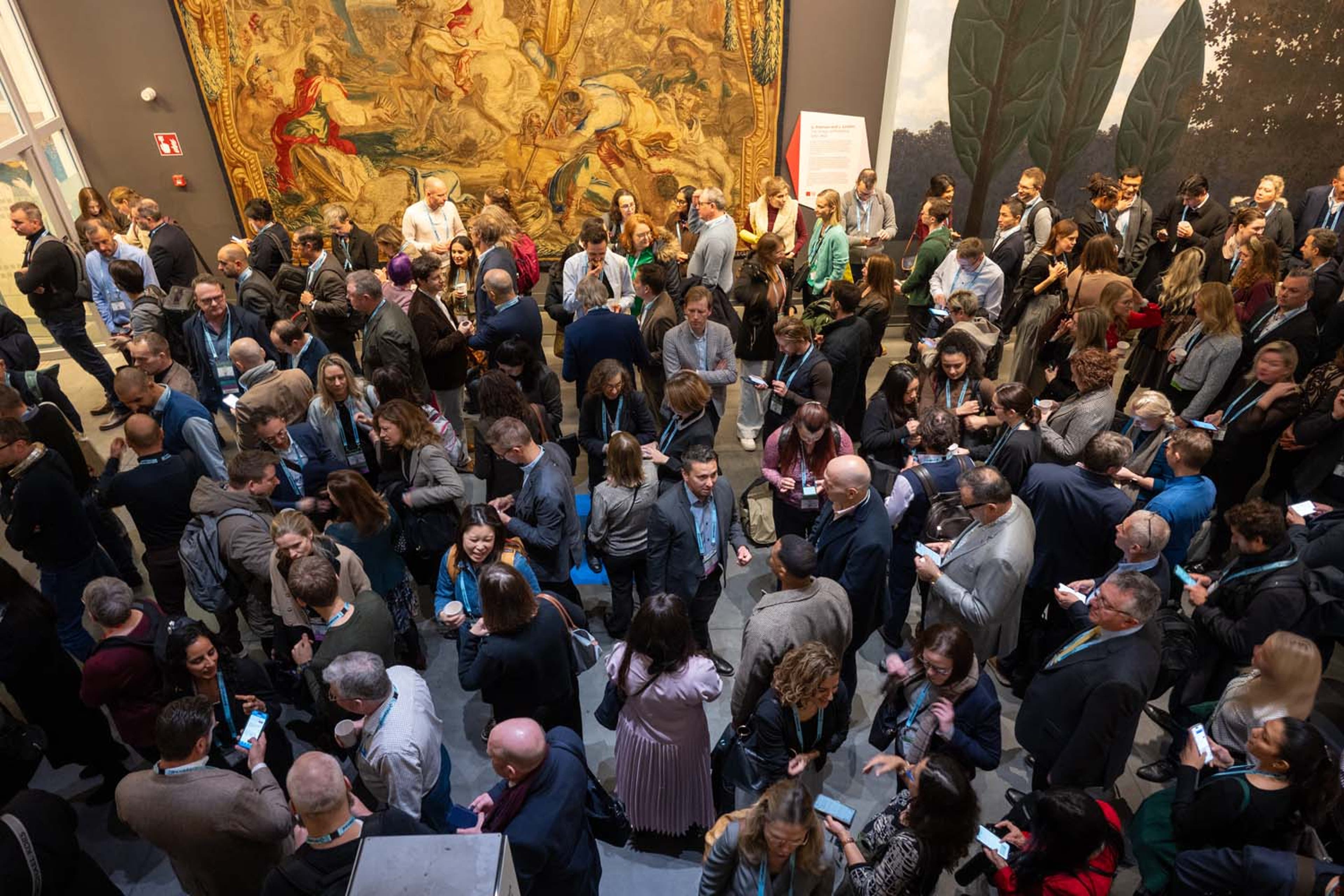 Large crowd gathered in a gallery space with ornate wall art, engaged in conversation during a networking event.