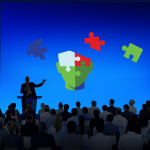 Graphic of a person speaking in front of people and puzzle pieces floating in the air.