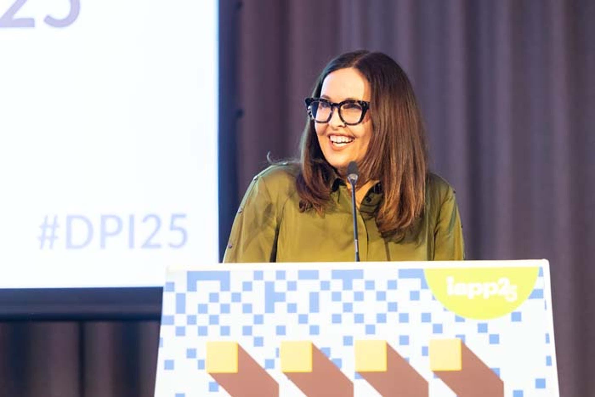 A woman in a green shirt and glasses speaking at a podium