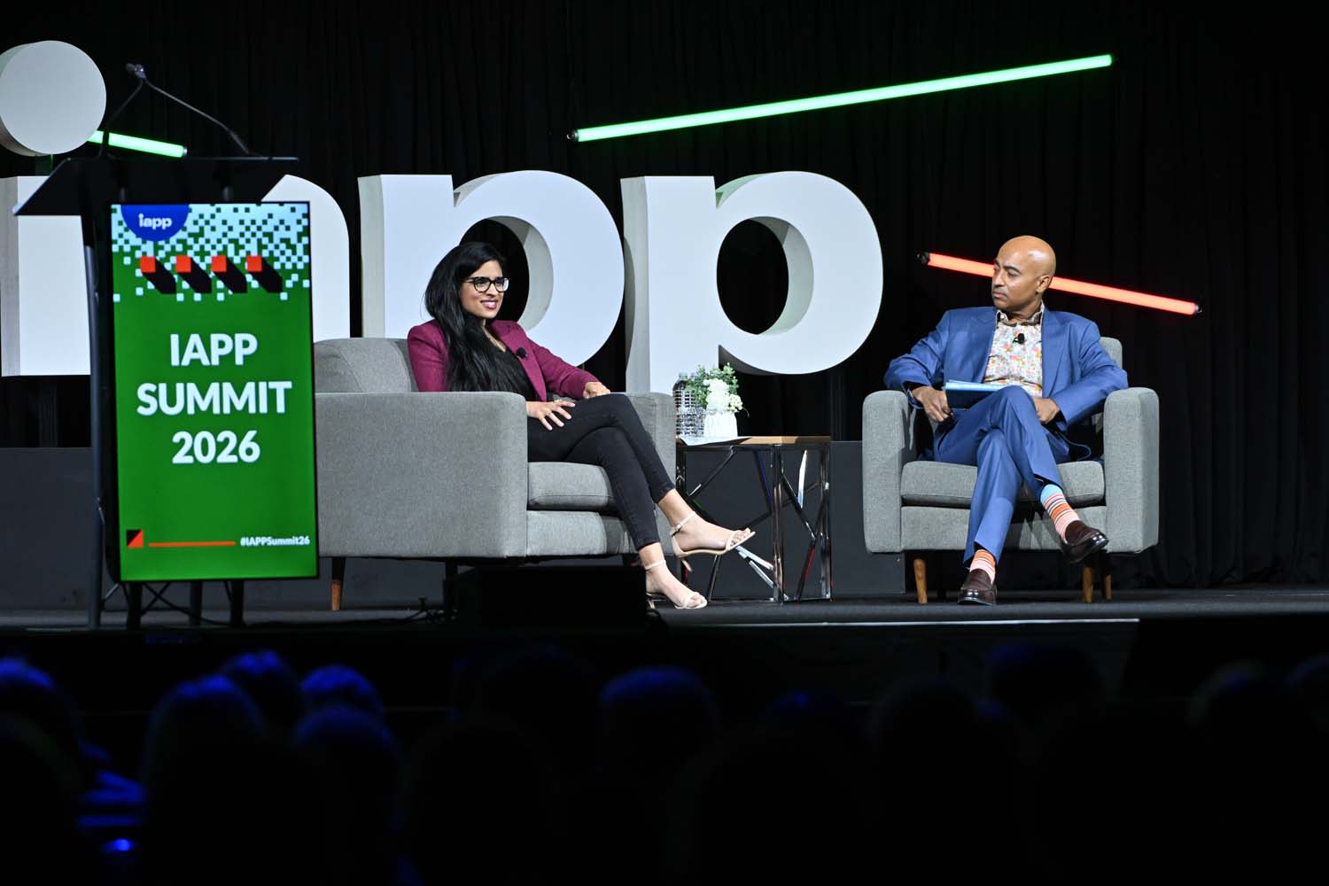 A closer view of the Spotlight Stage shows two seated speakers framed by stage lighting and a vertical sign reading IAPP Summit 2026 positioned at the edge of the stage.