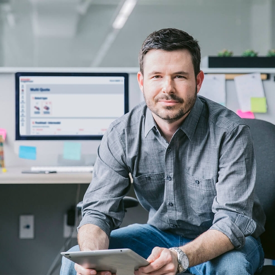 a person sitting in a desk chair holding a tablet with a computer in background
