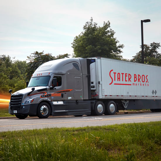 A large semi-truck on the road, with trees lining the highway under a clear sky