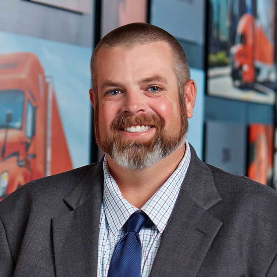 Man in a suit and tie standing in front of a wall displaying various truck images