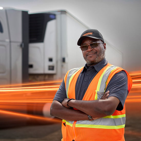 Truck driver wearing safety vest standing in front of refrigerated trailer