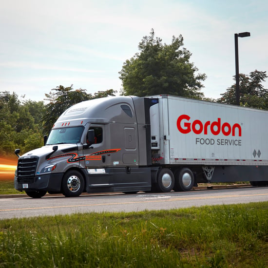 A large semi-truck on the road, with trees lining the highway under a clear sky