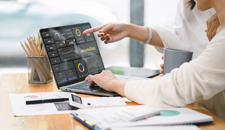 two people at a workstation analyzing graphs on a laptop screen