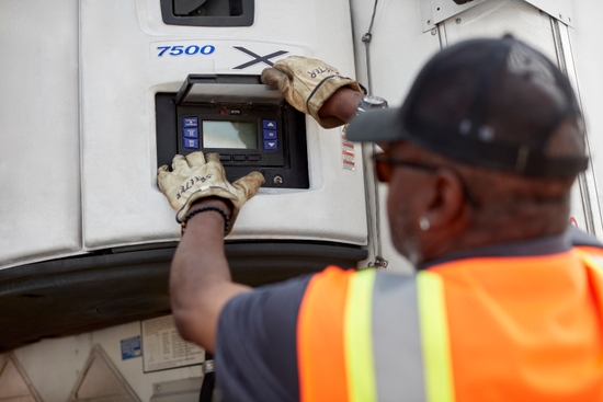 Looking over a man's shoulder while he adjusts the temperature controls on a refrigerated trailer.