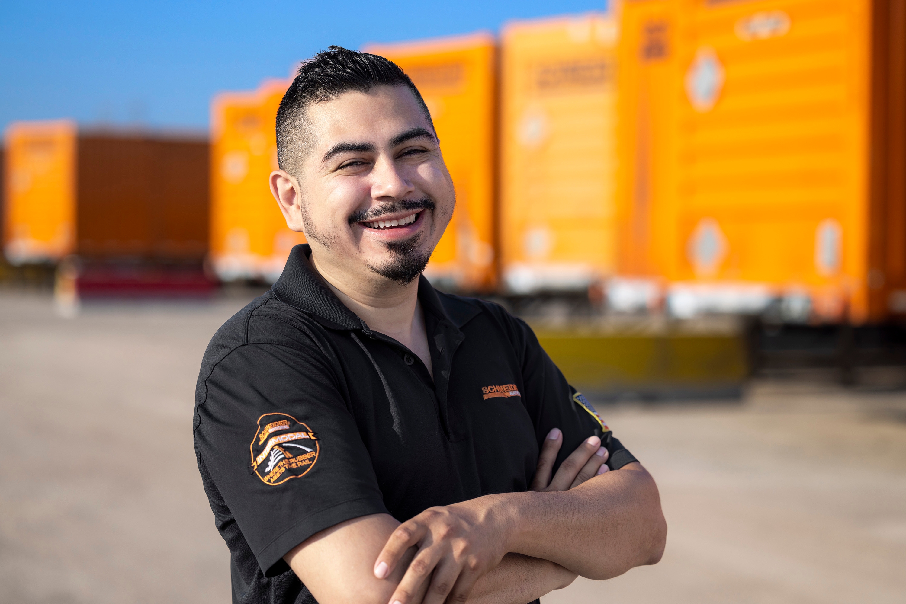 Image of Jonathan, an intermodal driver, standing in front of orange shipping trucks