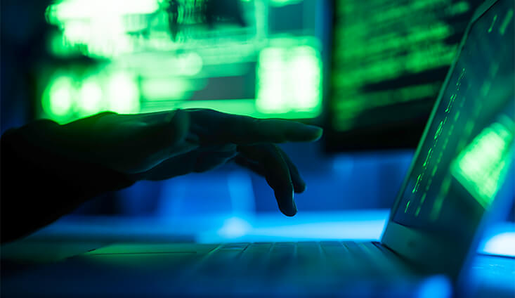 Shadow of a hand over a keyboard with blue and green lights in the background