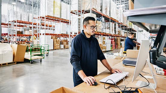 e-commerce_logistics_hero.jpg A person standing in front of a computer inside a warehouse.