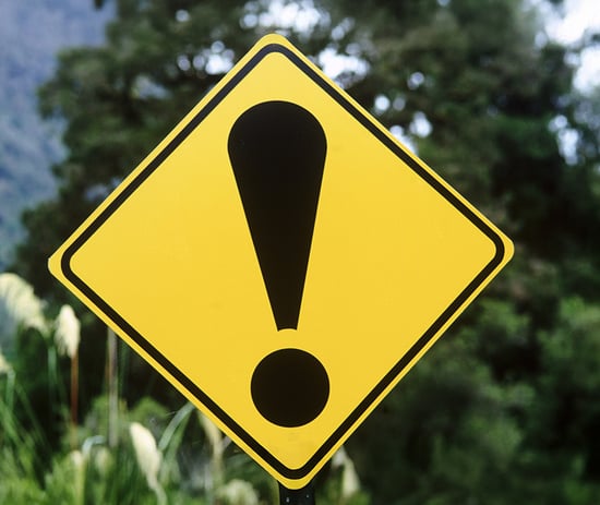 A yellow road sign with a black exclamation point