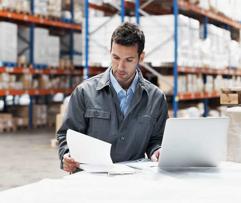 man in grey coat reviewing dynamic pricing solutions as he stands in front of a computer in a warehouse setting